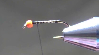 Hook secured in vise with an orange fluoro bead near the eye; black thread wraps laid down along the shank.